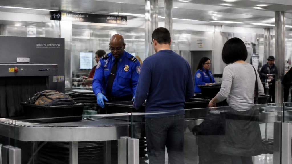 Airport security screening with passengers placing cabin baggage on the X-ray conveyor belt.